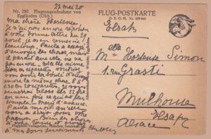 Schwarz-weiße Flugzeugaufnahme des oberbayerischen Dorfes Egglkofen (Obb.) aus der Vogelperspektive, um 1920: Zu sehen sind die Kirche mit schlankem Zwiebelturm, der angrenzende Friedhof, traditionelle Bauernhöfe und eine Bahnlinie inmitten sanfter Hügellandschaft. Herausgegeben als „FLUG-POSTKARTE" der Flugphoto Verlags-Ges. München unter Nr. 280 – ein frühes Luftbild und postgeschichtlicher Beleg der Nachkriegszeit, gelaufen 1920 nach Mülhausen im Elsass.