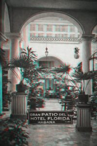 Kuba Ansichtskarte von 1907 mit dem Gran Patio des Hotel Florida in Havanna: ein kolonialer Innenhof mit tropischen Palmen, klassischen Säulen, großem Torbogen, schmiedeeisernem Kronleuchter und Sitzmöbeln; am linken Rand ein handschriftlicher Abschiedsgruß in Schreibschrift. Die Rückseite zeigt das kubanische Staatswappen, eine grüne 1-Centavo-Briefmarke mit Habana-Poststempel von 1907 sowie die Adresse an Mr. James Sweeney in Atlantic City, New Jersey. Ein Embargo-Sammlerstück zur transatlantischen Postgeschichte und ein Beispiel für einen Sammlungsreport.
