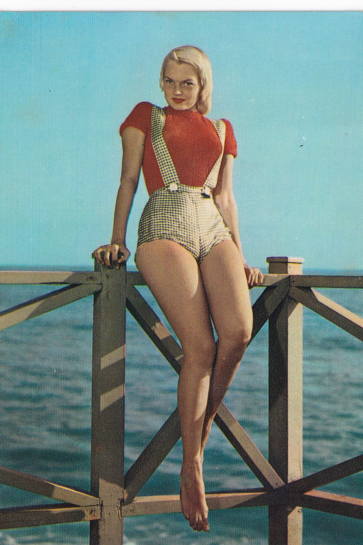 Originale Pin-up-Ansichtskarte aus der Sammlung von Igor Adolph: Frau im roten Oberteil und karierter Hose vor dem Wasser